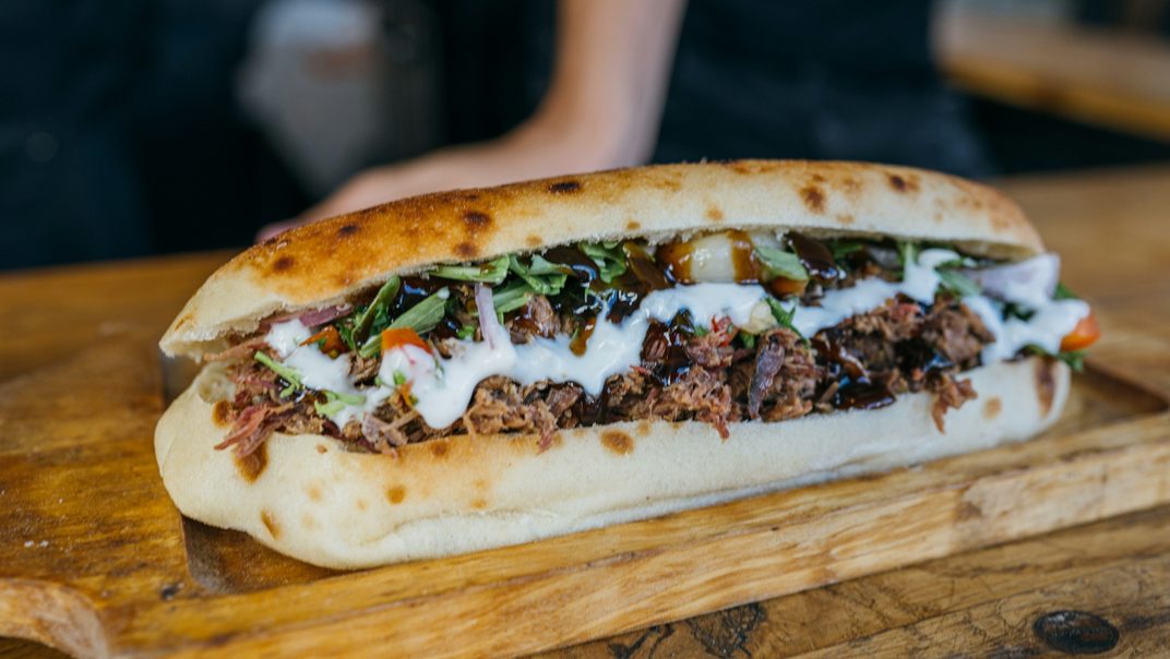 A shredded beef sandwich on a grilled roll, on a wooden board