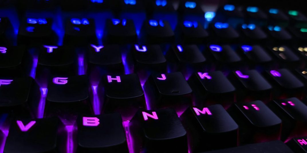 Backlit mechanical keyboard glowing purple and blue in the dark