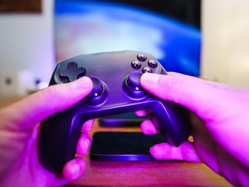 Two hands holding a game controller under purple light