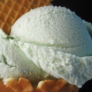 Two scoops of pale green pistachio gelato in a waffle cone