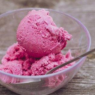 Pink strawberry gelato in a glass bowl with a spoon