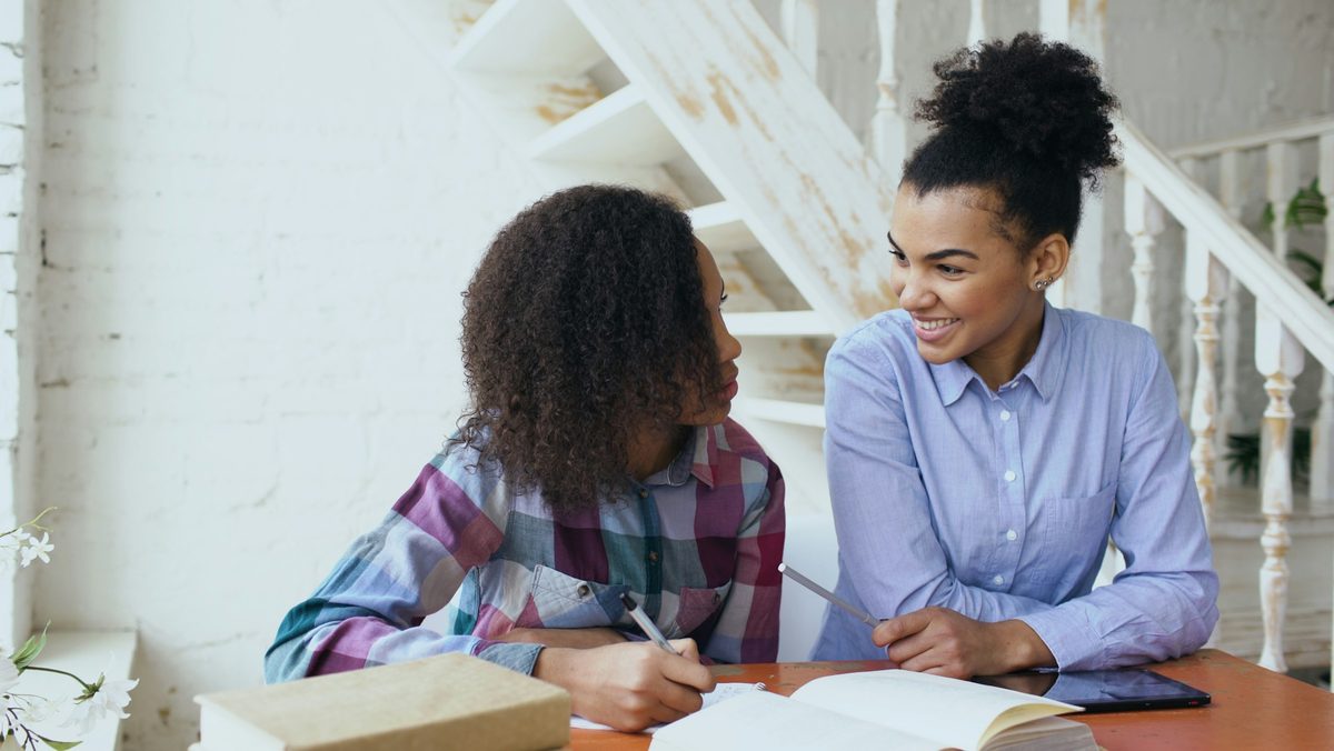 A tutor and a student working through a workbook together at a table