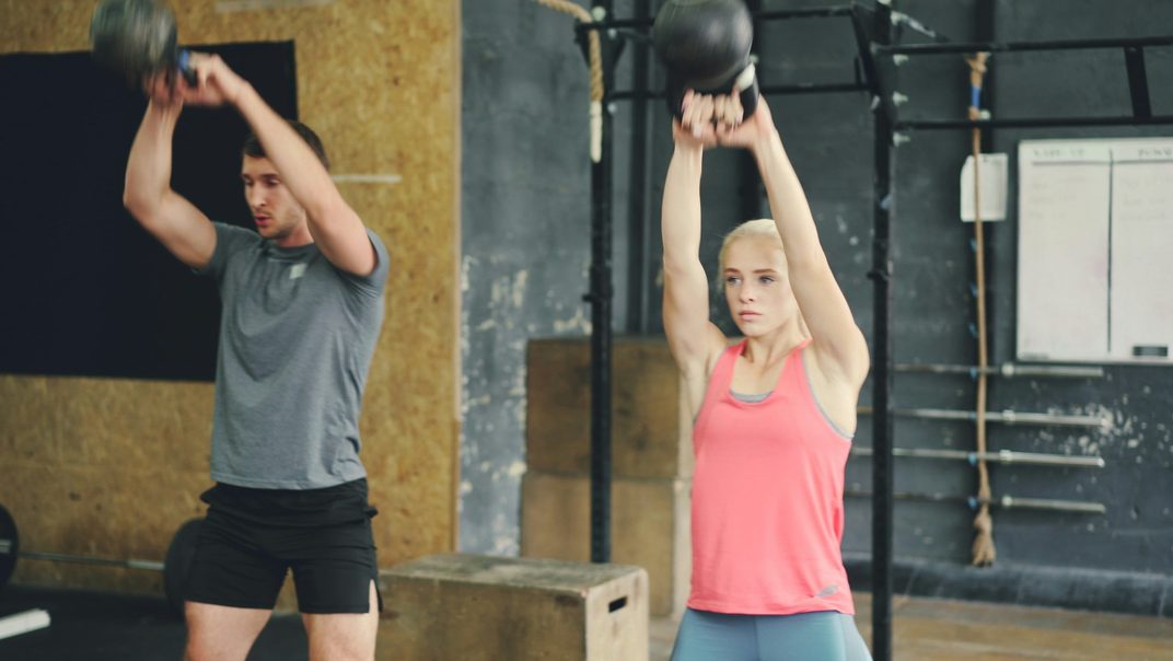 A man and a woman doing kettlebell swings on the gym floor