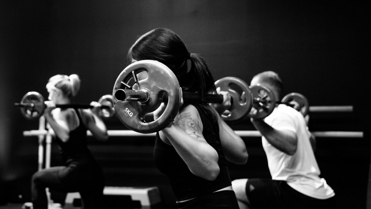 Three members lifting barbells in a black and white gym