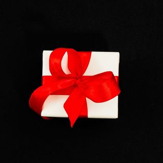 A small white gift box tied with a red ribbon on black