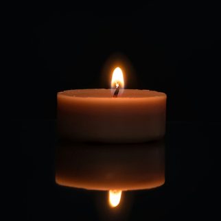 A lit pillar candle on a black table, reflected below