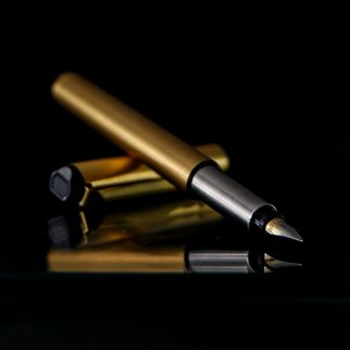A brass pen resting on its cap on black