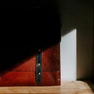 A red-brown leather case with a dark strap in a shaft of light