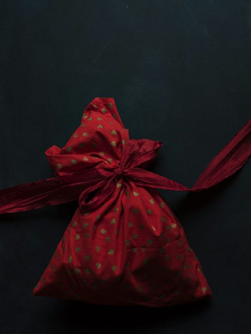 A gift in deep red patterned cloth tied with a ribbon on black