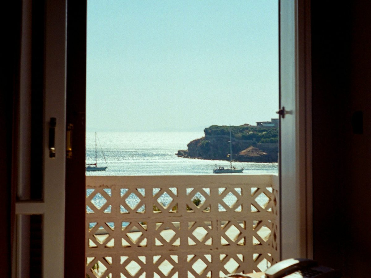 An open balcony door looking out to a calm sea and a rocky headland