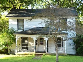 A white clapboard house with a front porch, framed by trees