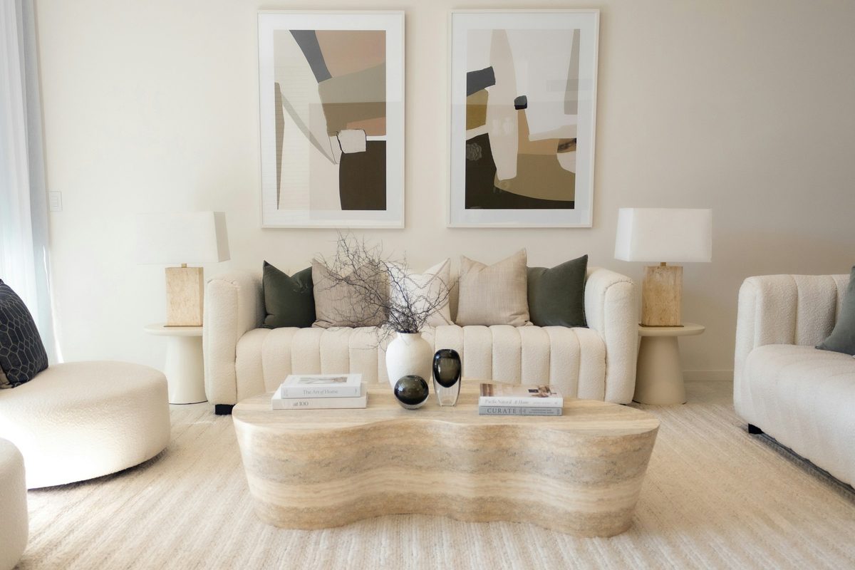 A calm living room in warm whites with a curved sofa and two abstract prints