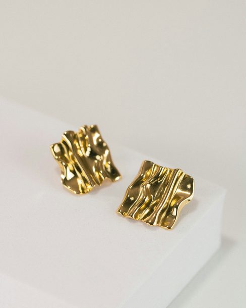 A pair of rippled gold earrings on a white block
