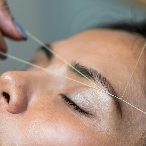 A brow artist shaping a client's brows with thread