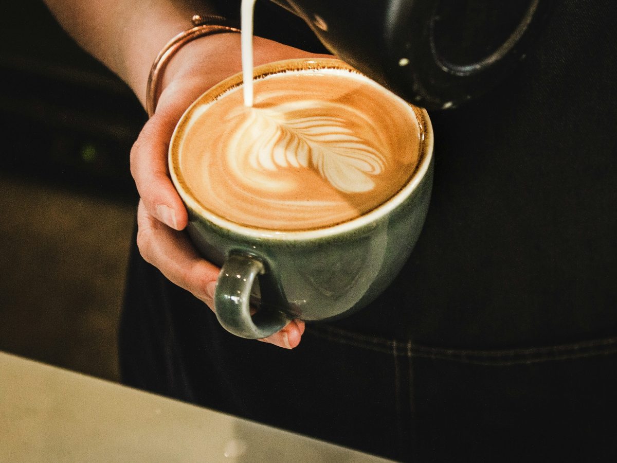 A barista pouring steamed milk into a cup to draw a rosetta