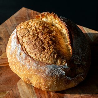 A round crusty sourdough loaf on a wooden board
