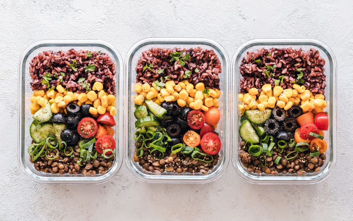 Three glass meal-prep containers of grains, corn, tomatoes and greens