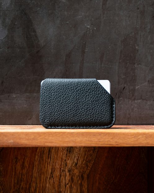 A black leather card case on a wooden plinth against a dark wall