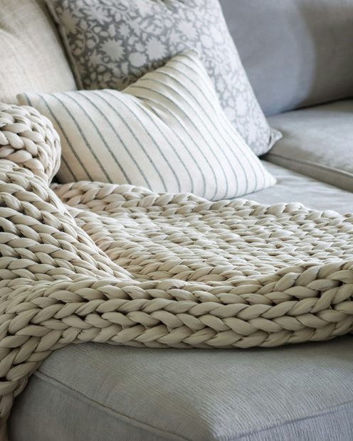 A chunky knit throw over the arm of a gray sofa