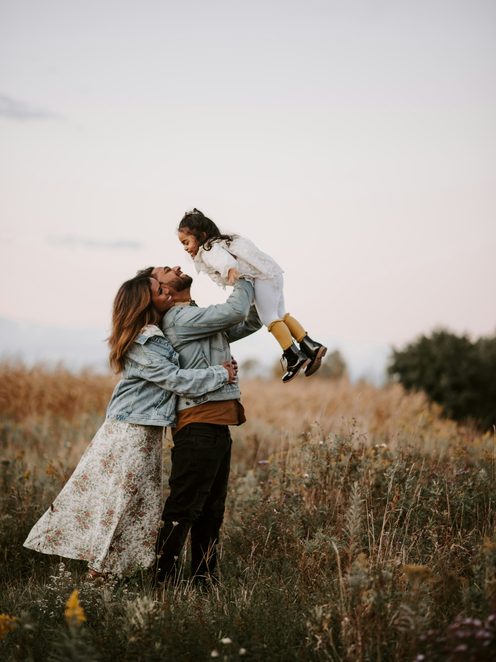 A mother lifting her daughter into the air in a tall-grass field