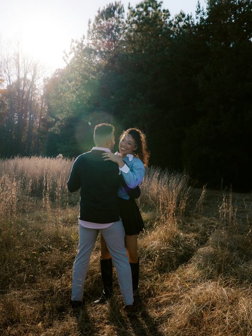 A couple embracing in a sunlit field at the edge of a wood