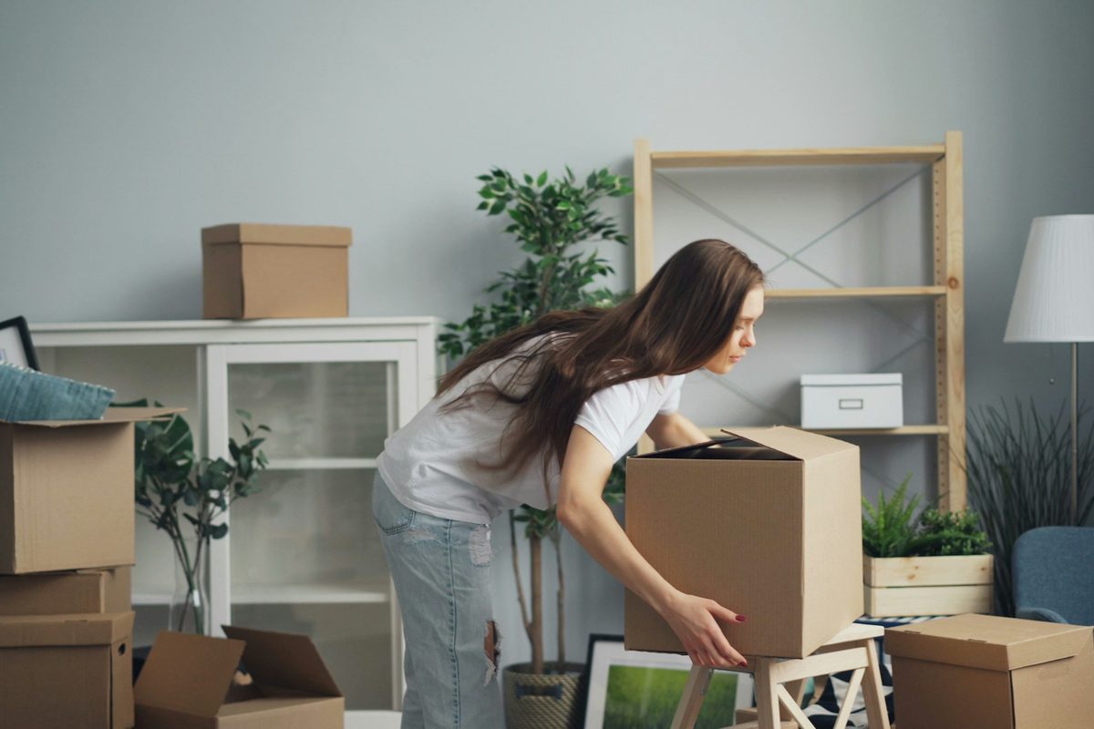 A woman packing cardboard boxes in a bright living room