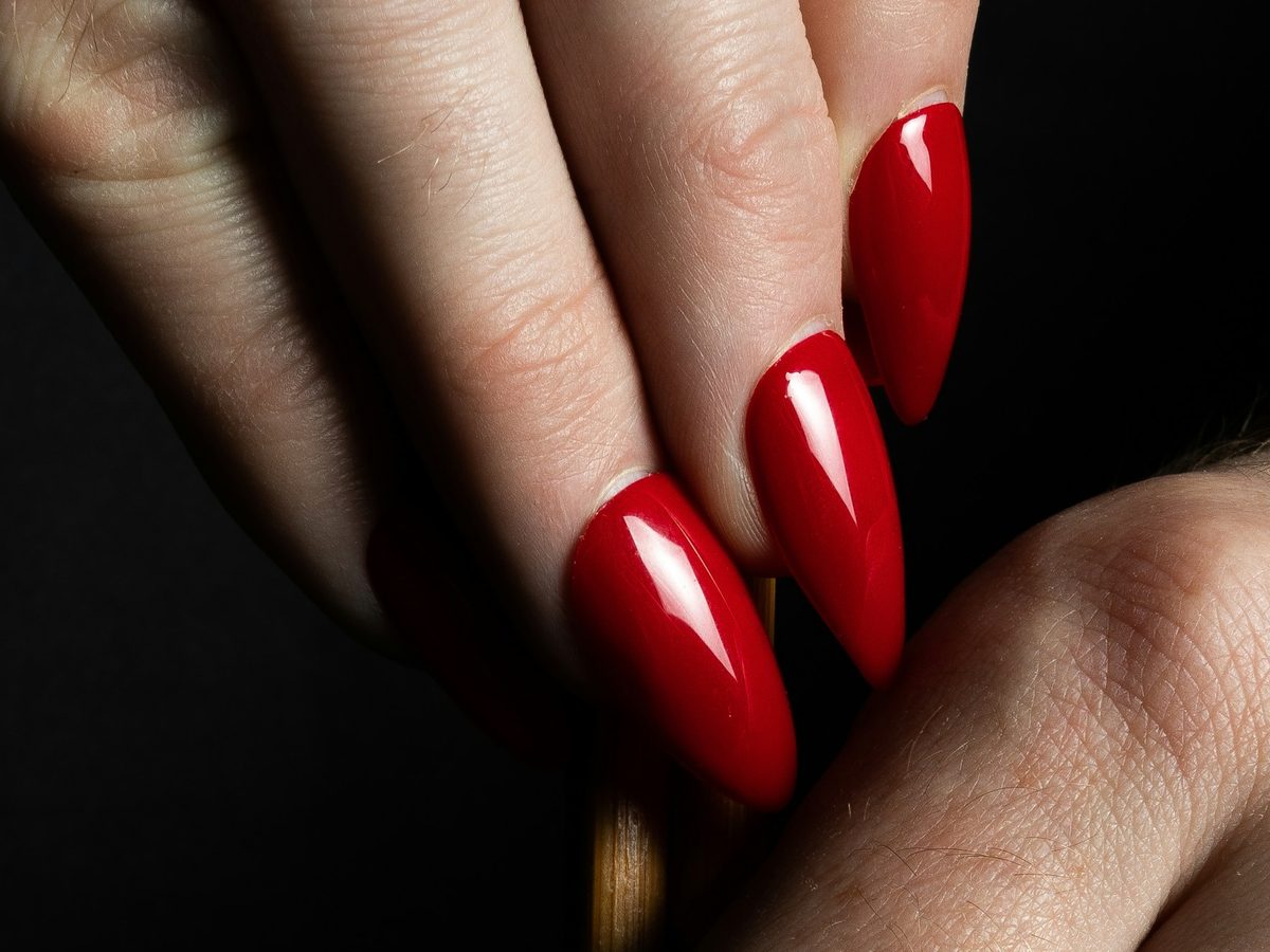 A hand with long glossy cherry-red almond nails against a black background