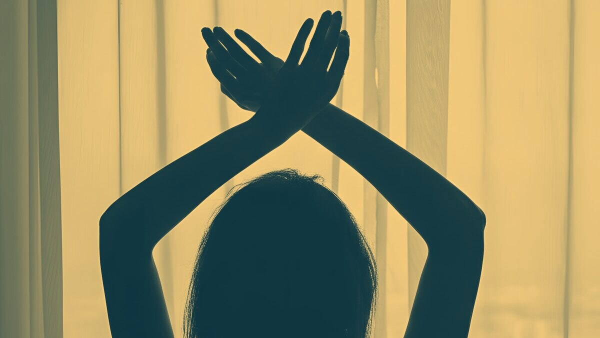 Silhouette of a woman stretching with her arms crossed overhead by a bright window