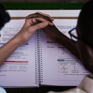 Two people's hands on an open workbook