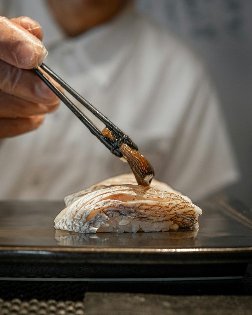 A chef brushing soy over a piece of nigiri
