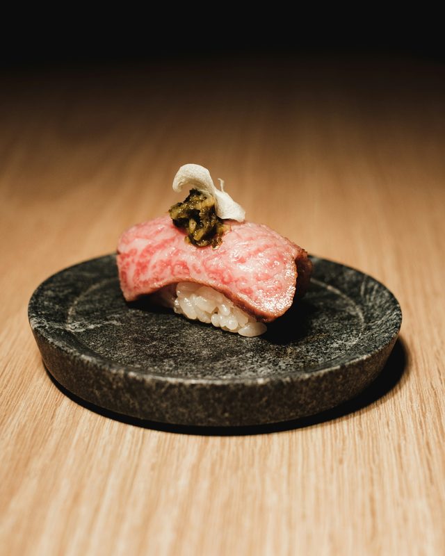 A single piece of nigiri on a dark stone plate