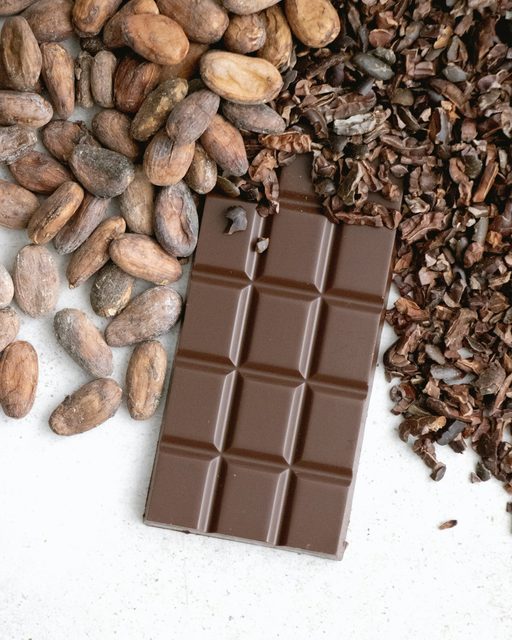 A dark chocolate bar beside roasted cacao beans and nibs