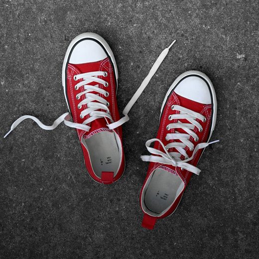 A pair of red canvas sneakers on gray concrete, seen from above