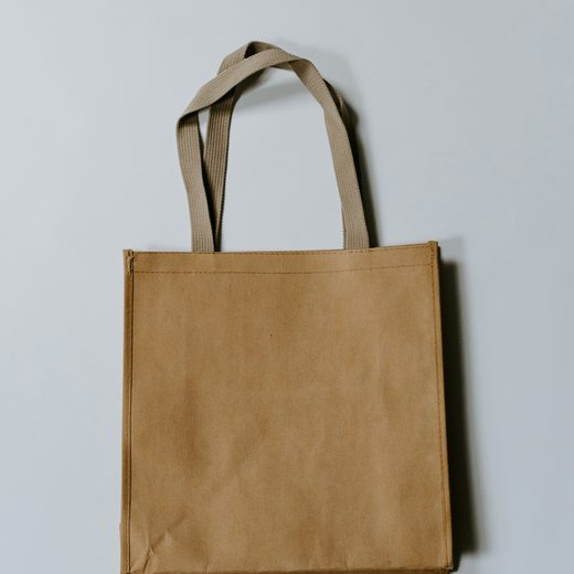 A plain tan canvas tote bag on a pale gray ground