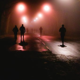 Figures walking down a foggy street at night under red lights
