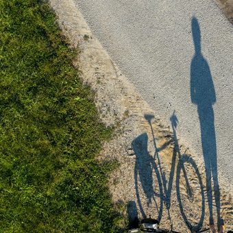 The long shadow of a person and a bicycle on a gravel path