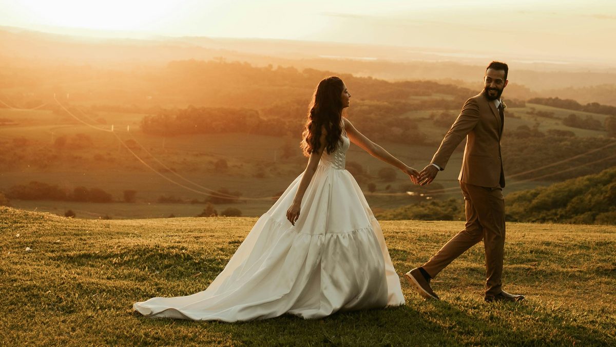 A couple walking hand in hand across a hilltop field at sunset