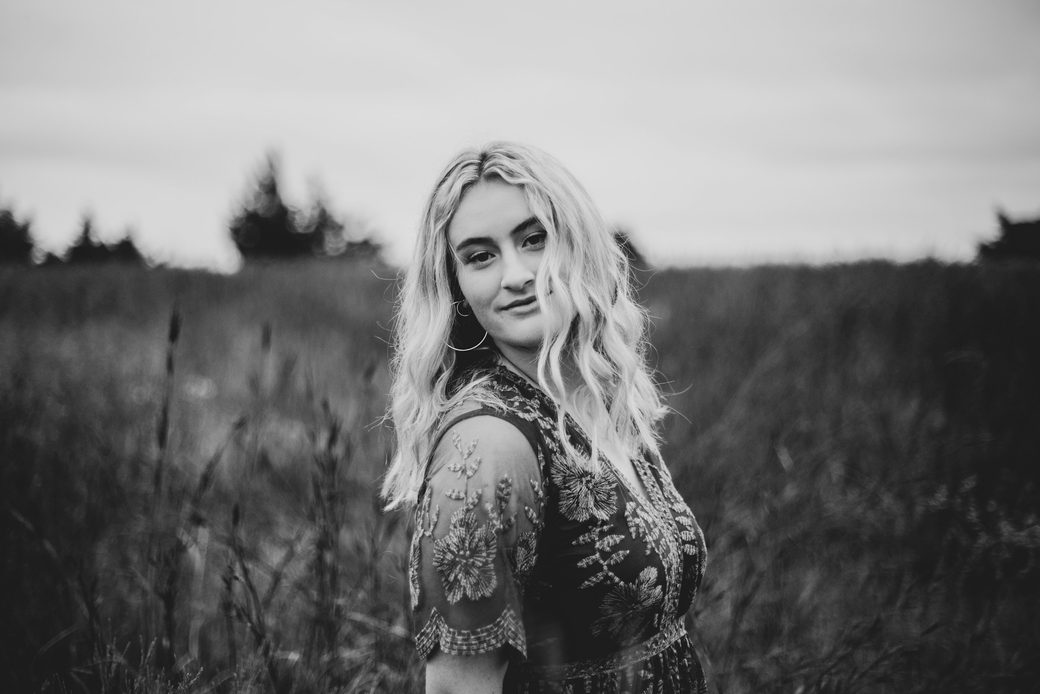 A woman with long hair standing in a field of tall grass, in black and white