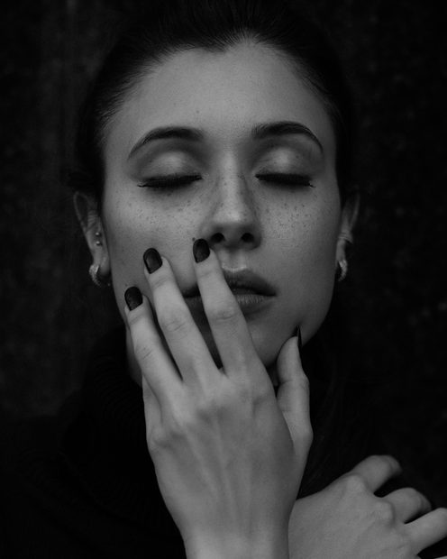A woman with closed eyes resting her hand against her face in soft light