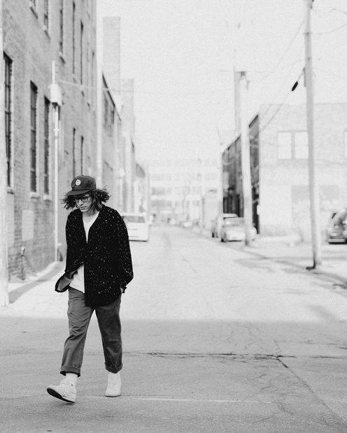 A man in a hat walking across an empty street lined with brick buildings