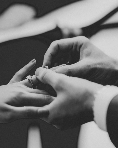 A groom sliding a ring onto a bride's finger, in black and white