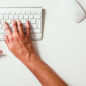 Hands typing on a white keyboard on a bright desk