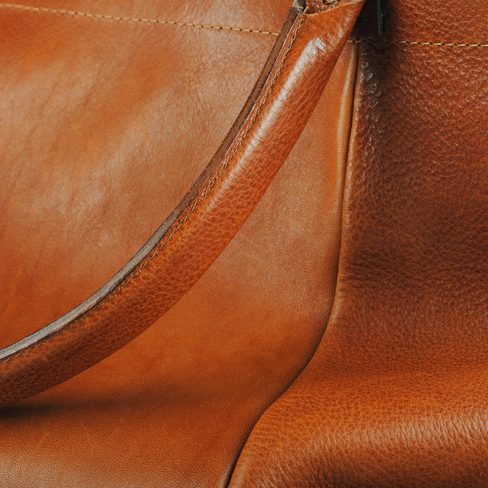 Close-up of a strap curving over soft brown leather