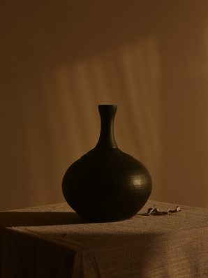 A round black bottle vase on a linen-covered table