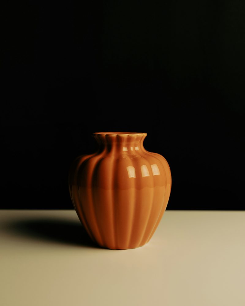 A fluted terracotta vase on a pale table against a black backdrop