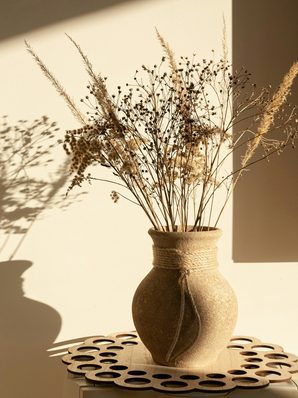 A stoneware vase of dried grasses casting a shadow on a warm wall