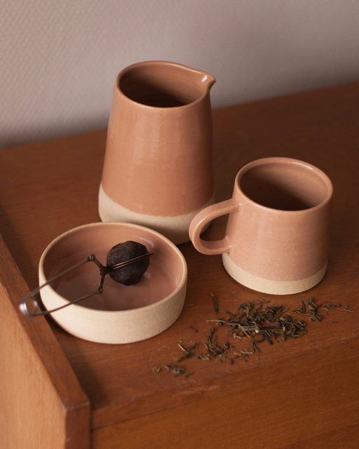 A blush stoneware pitcher and cup on a wooden counter