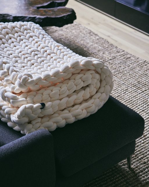 A chunky cream knit throw folded over the arm of a dark sofa
