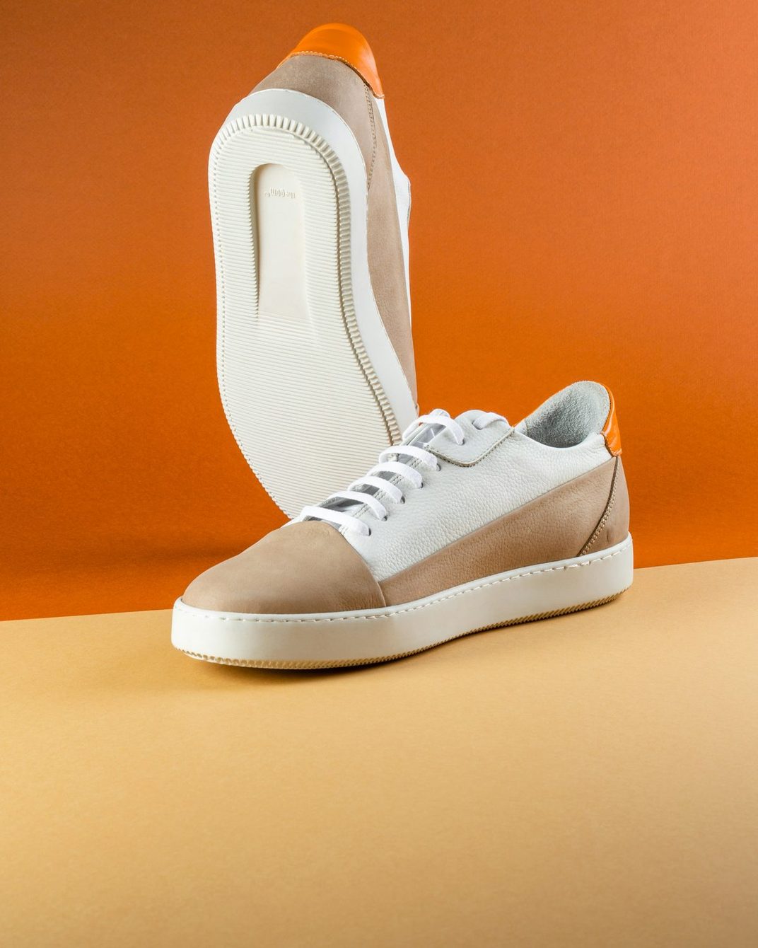 A pair of white and tan leather sneakers posed against an orange backdrop