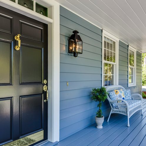 A painted front porch with a black door and a wicker chair
